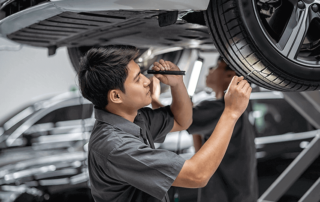 Automotive technician working underneath a car while holding a flashlight and looking at a tire